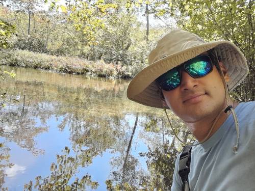 Carlos Morantes Ariza standing in front of a body of water for his study on invasive aquatic plants on Long Island.