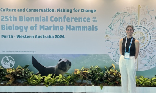 Chelsi Napoli standing in front of 25th Biennial Conference on the Biology of Marine Mammals poster
