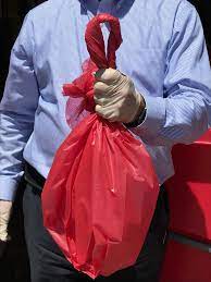 person wearing latex gloves holding the closed red bag in front of their body