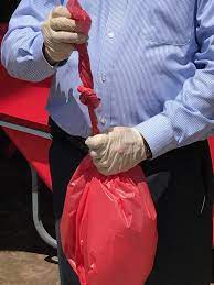 person wearing latex gloves tying a knot on the drawstring of a red bag to indicate that it is closed properly