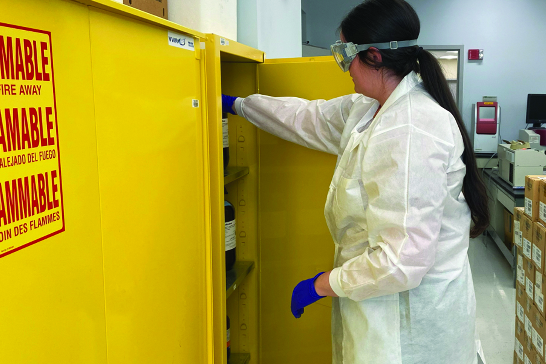 person in lab coat taking something from a flamibles cabinet