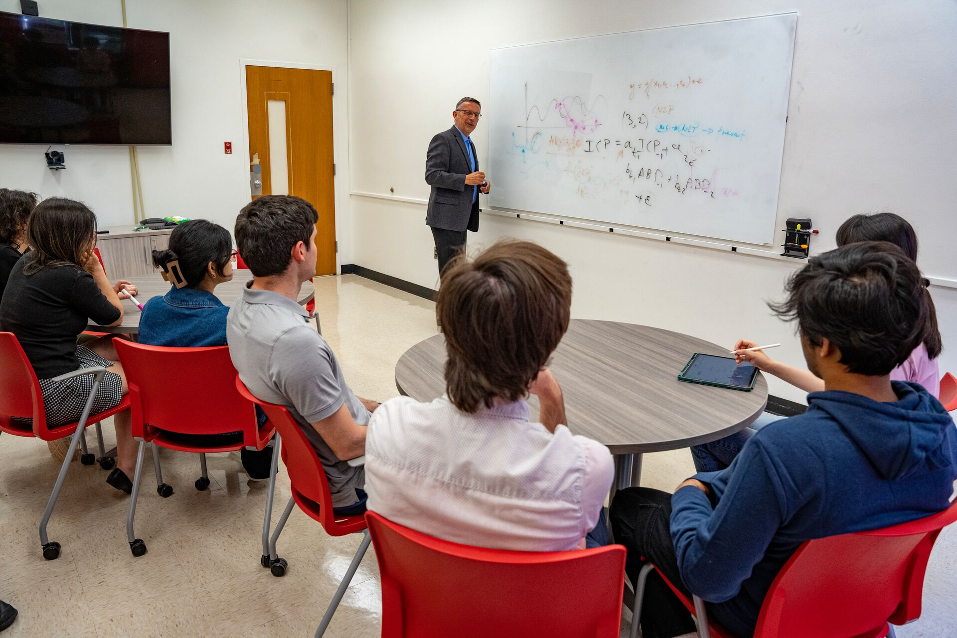 Professor giving a lecture to a class of multiple students, paying attention intently.