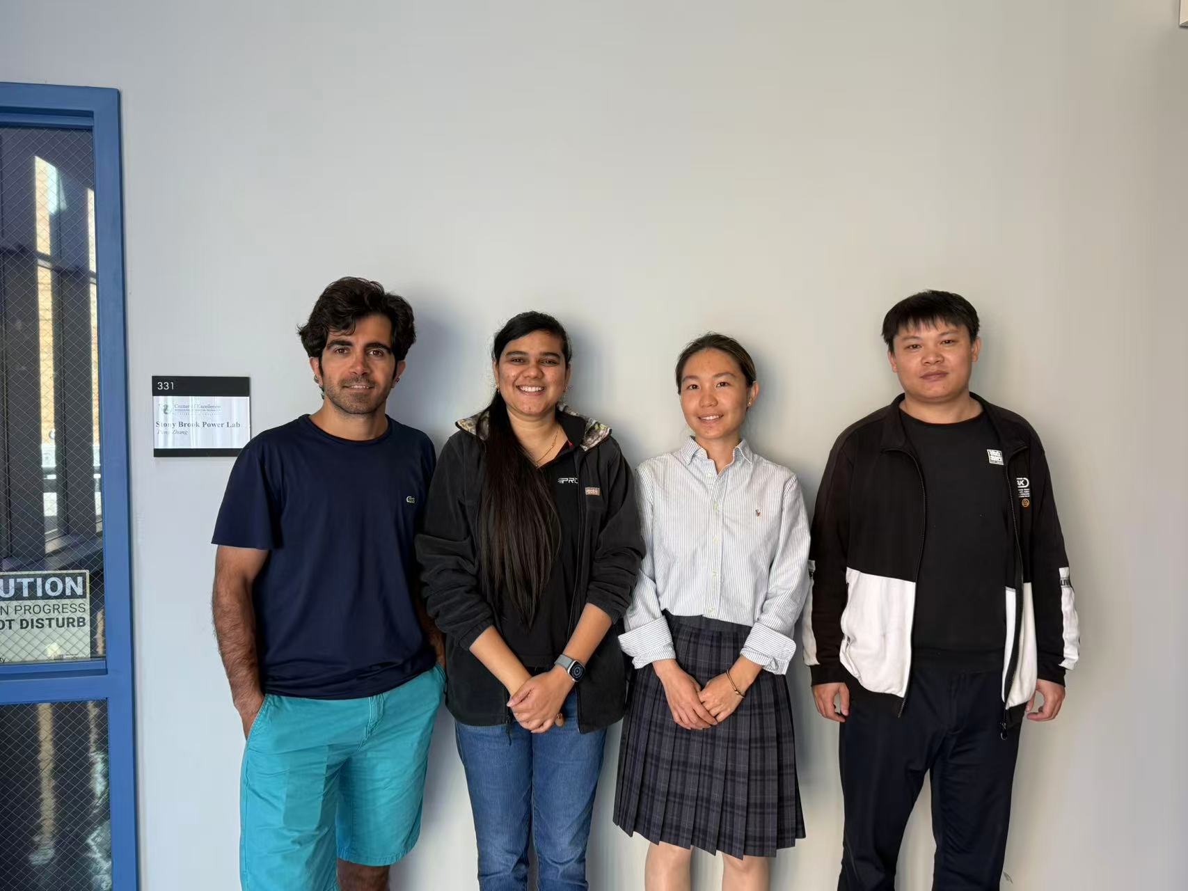 A group of four people stands in a line, posing and smiling, celebrating a group achievement. 