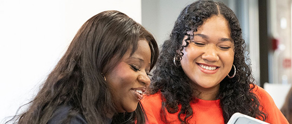 two female students smiling looking at ipad