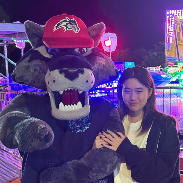 Maddy Zhu Girl standing with her arm linked with Stony Brook mascot, Wolfie