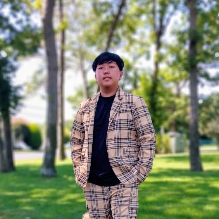 Ryder Min Boy in plaid shorts and suit jacket standing in a park with trees in the background