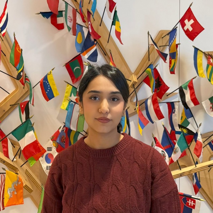 Somaya Aswadi Girl in a brown sweater standing in front of various country flags