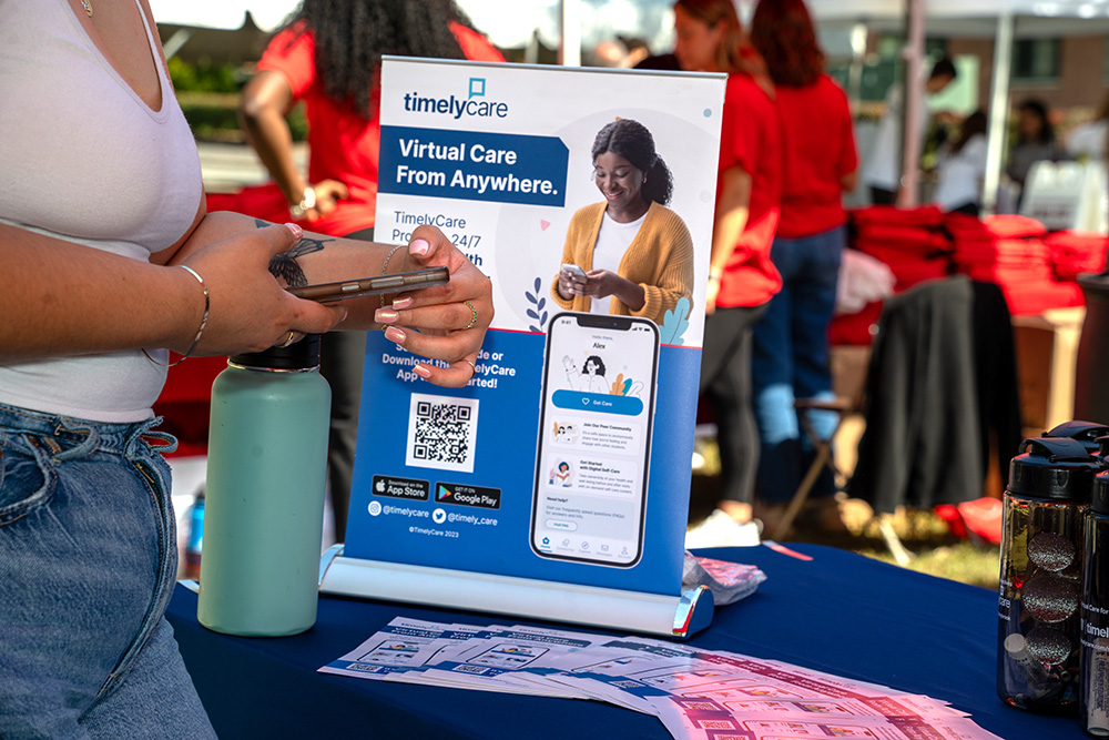 A woman holding a phone in front of an outdoor table with a Timelycare sign.