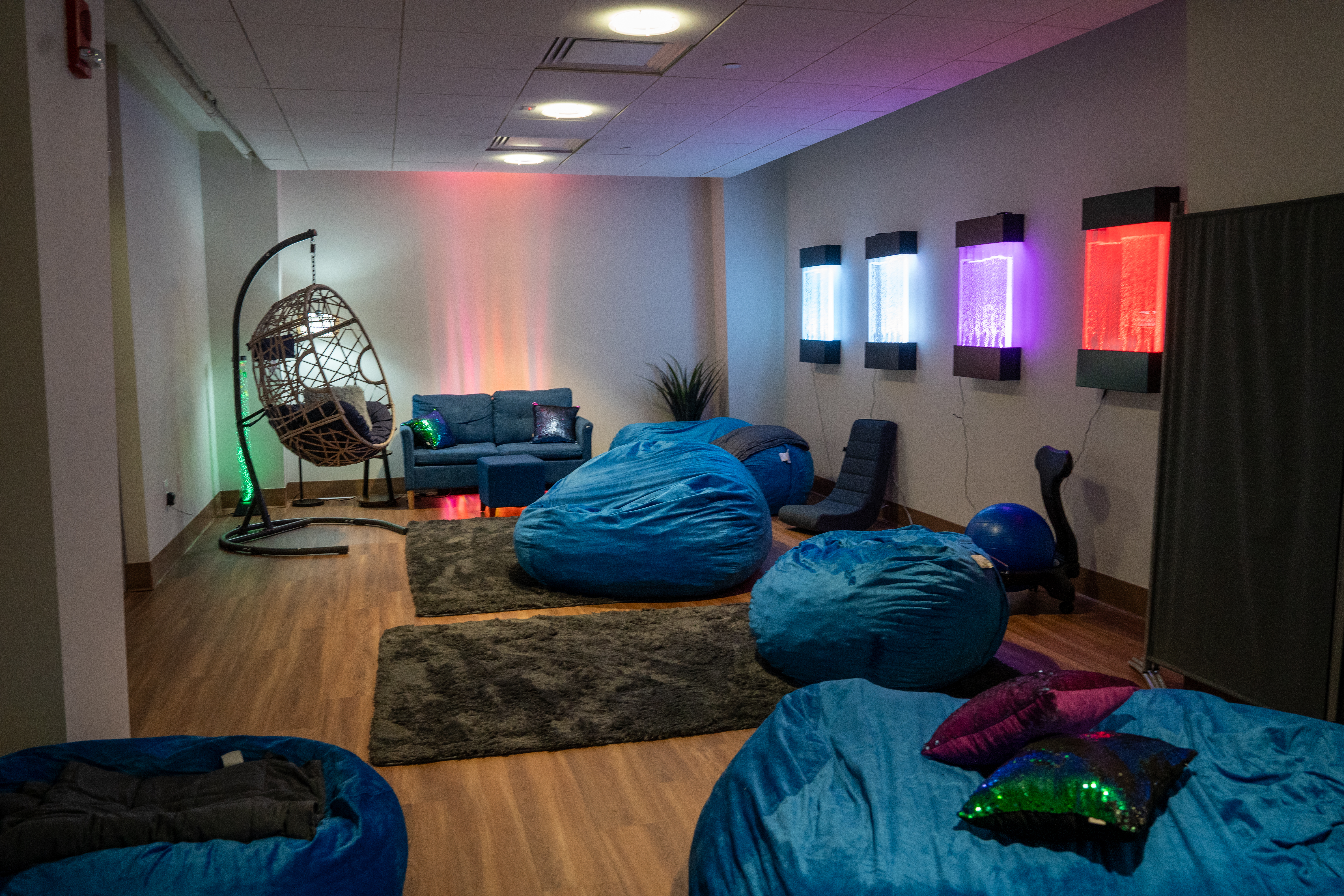 A room with blue bean bag chairs, soft lighting, and a hanging chair.
