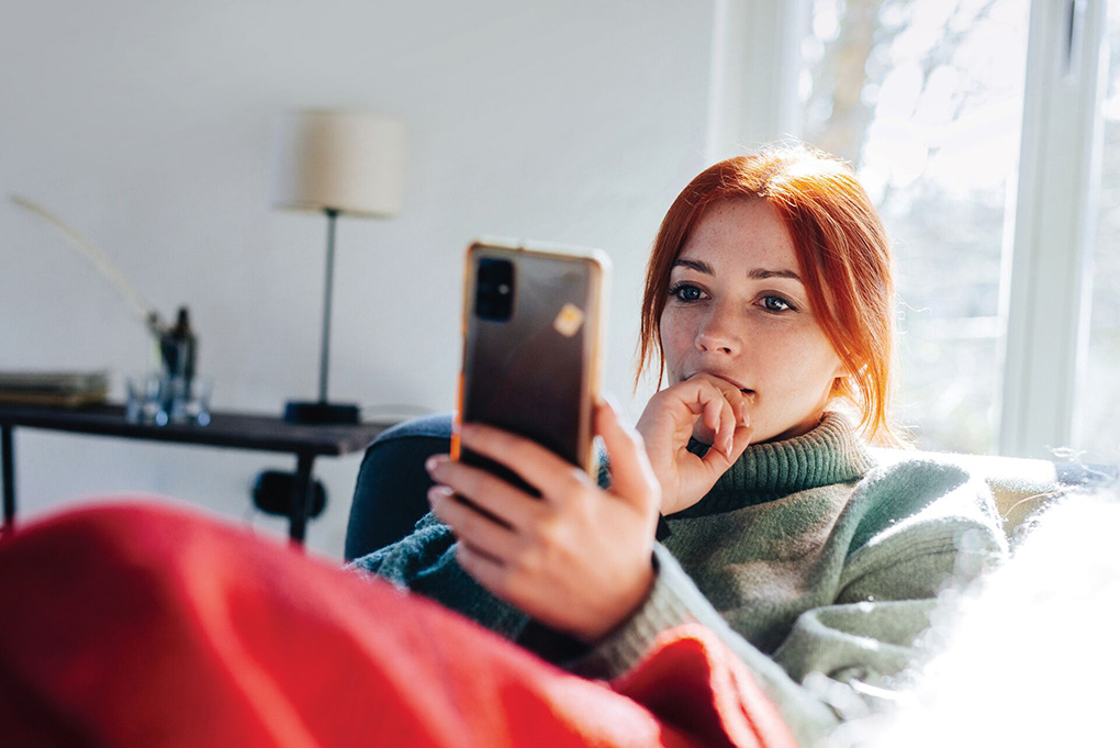 A girl with red hair holding and looking at her phone.