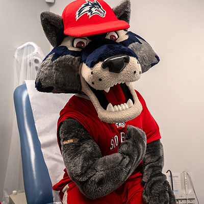 Wolfie in a doctor office chair flexing his arm to show off a bandaid.