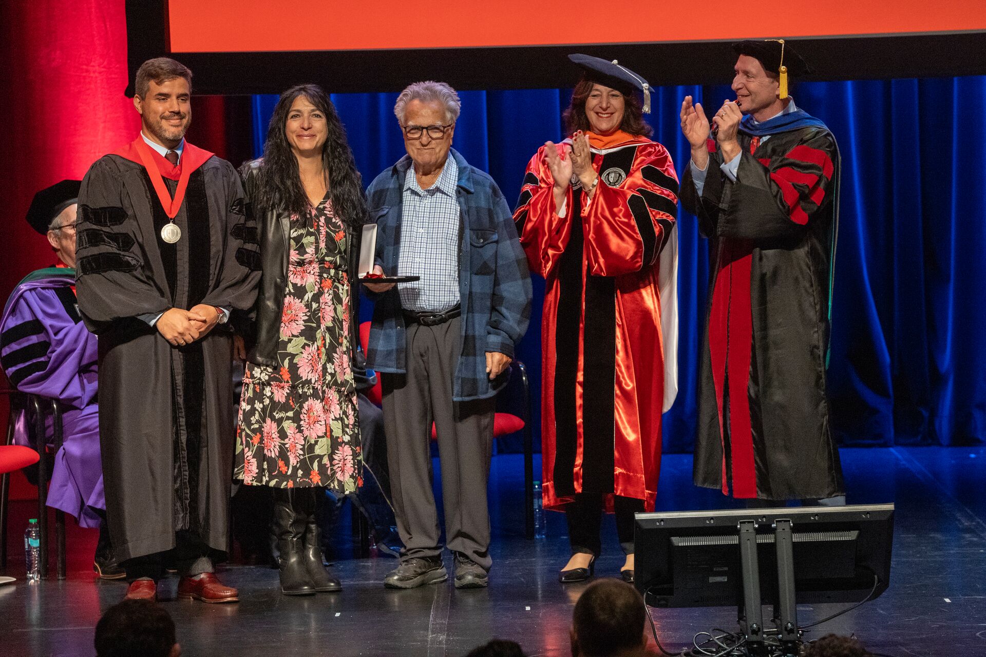 Group photo on a ceremonial stage, celebrating the installation of Simos Zenios as the current inaugural Peter V. Tsantes Professor in Greek Literature and Language.