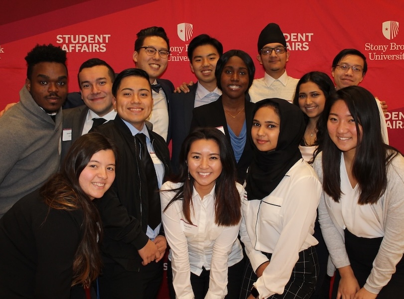 A group of HEA students specializing in student affairs posing in front of a Stony Brook Student Affairs step and repeat