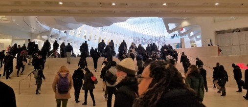 Commuters ascend a grand staircase in a bright, modern transit hub.