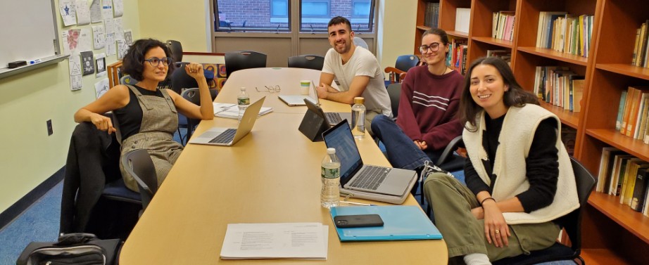 Four people sit around a large table in a library study room.