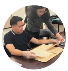 Two people wearing archival gloves examine historic documents together at a table.