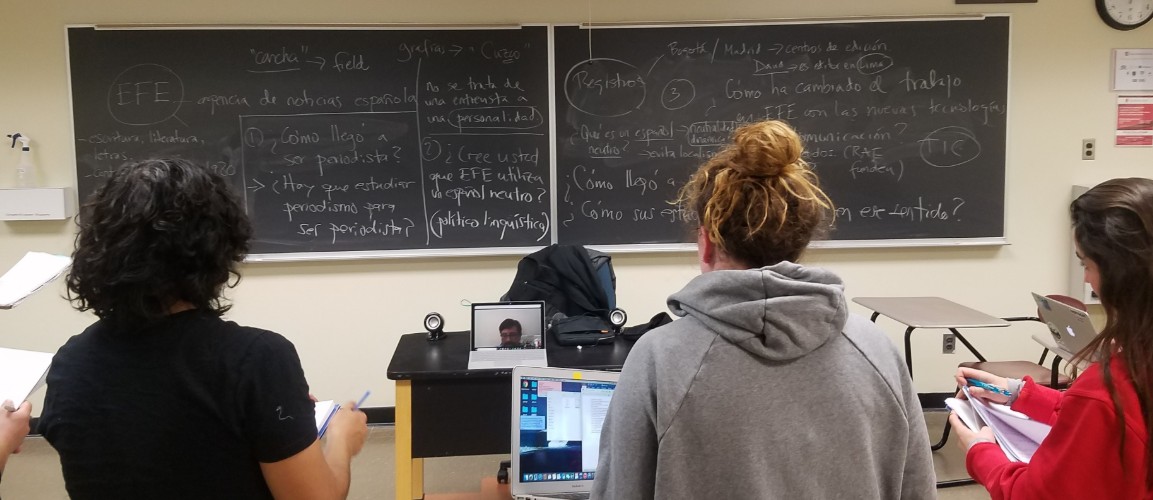 Students in a classroom engage with a remote guest speaker via laptop.