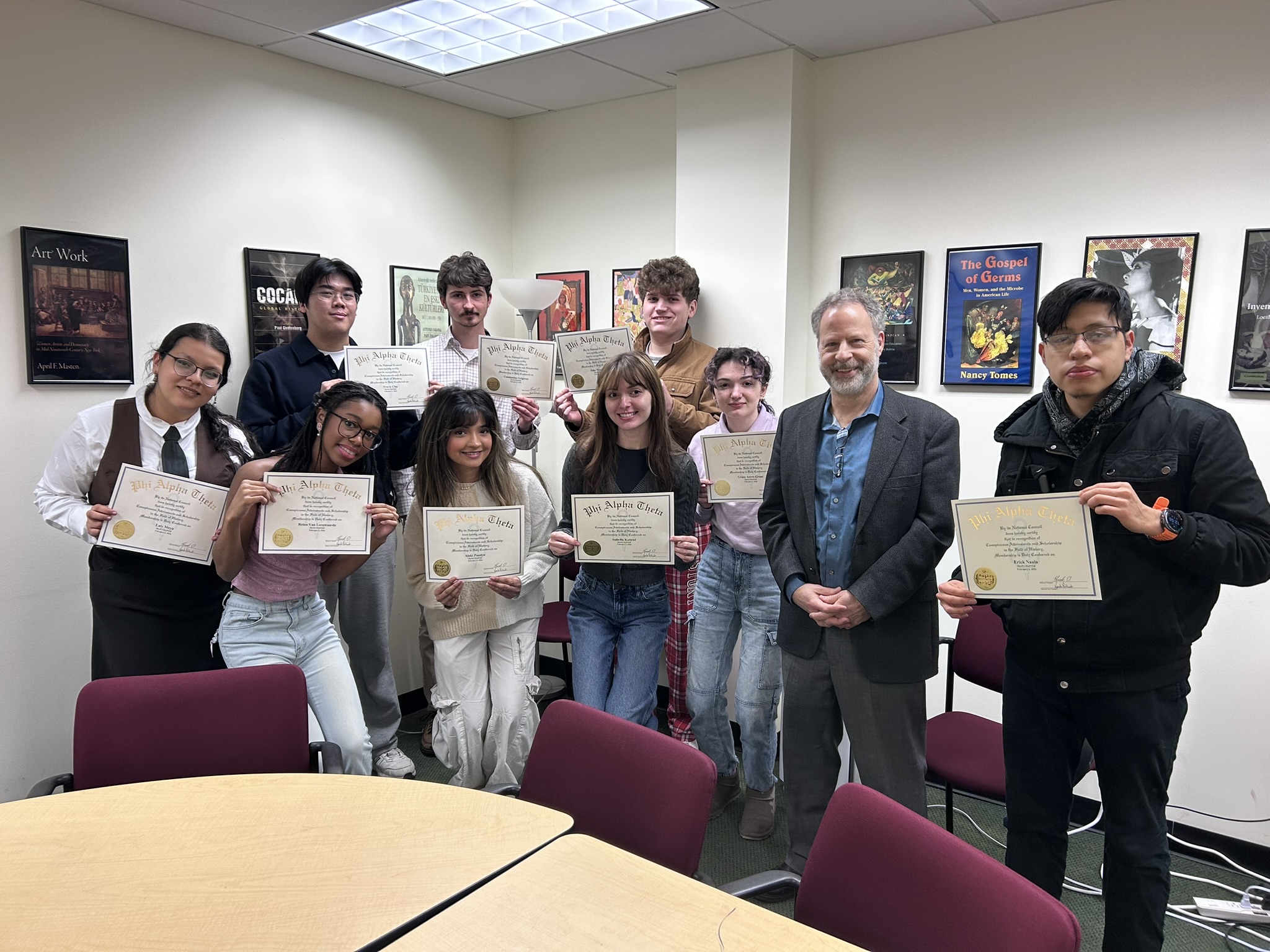 A group of people holding certificates in a room with framed posters, smiling.