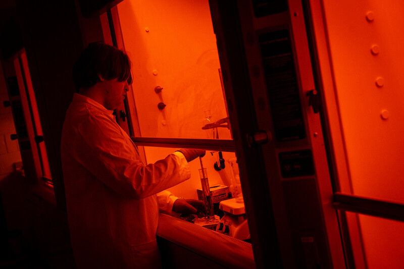 Researcher working at an orange-lit laboratory fume hood.