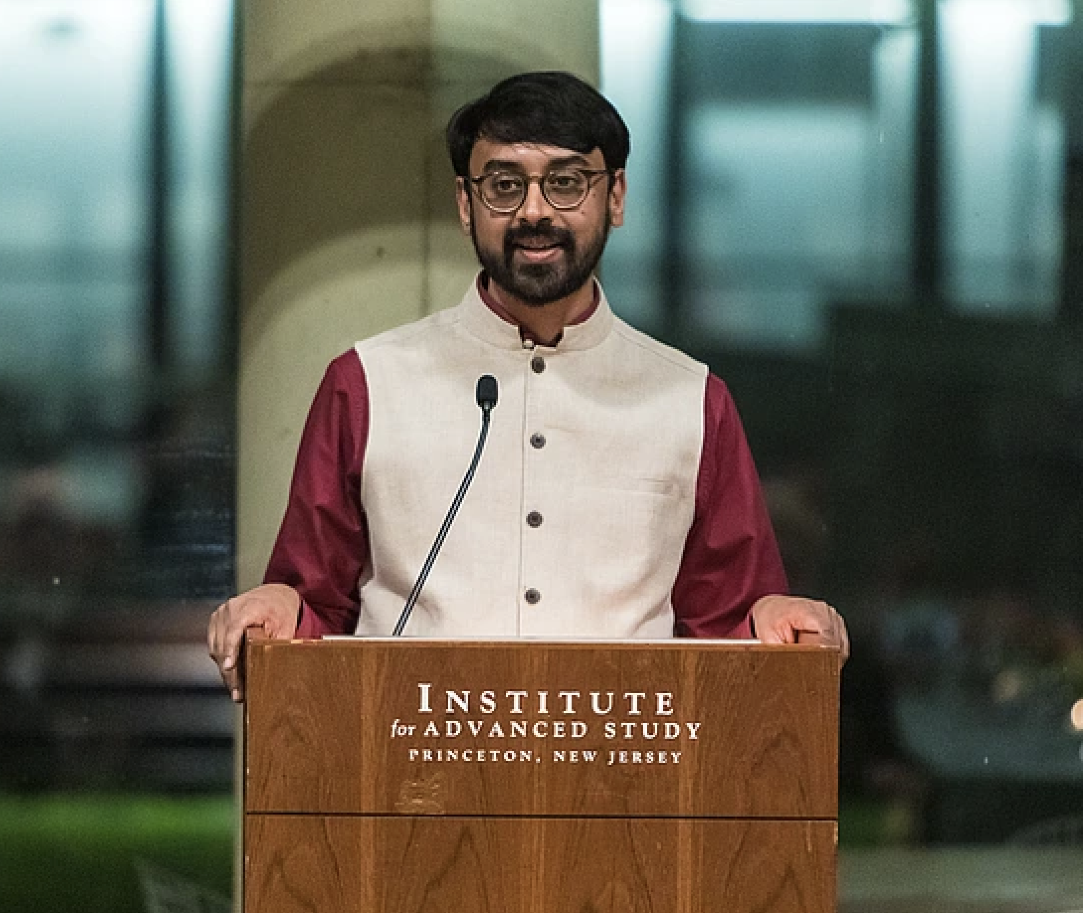 Manjul Bhargava speaking at a podium labeled "Institute for Advanced Study, Princeton University"