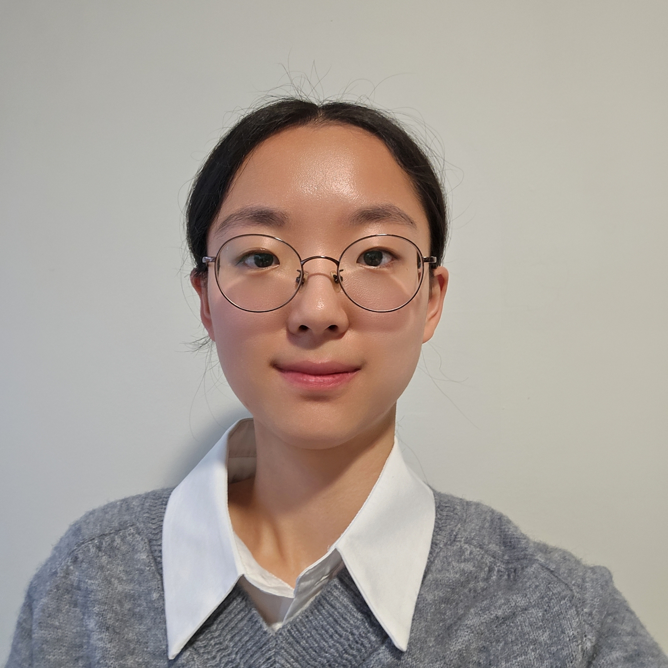 Girl with glasses and gray shirt smiles against a white wall