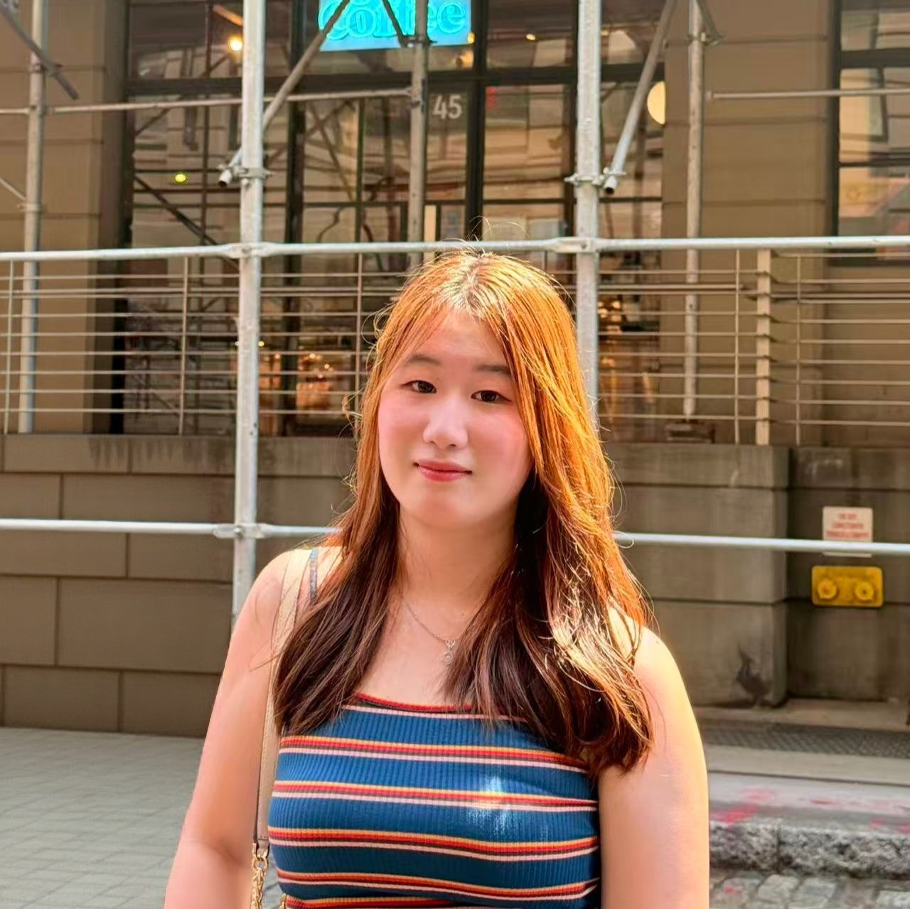 Girl with striped shirt and orange hair stands on street in front of city building