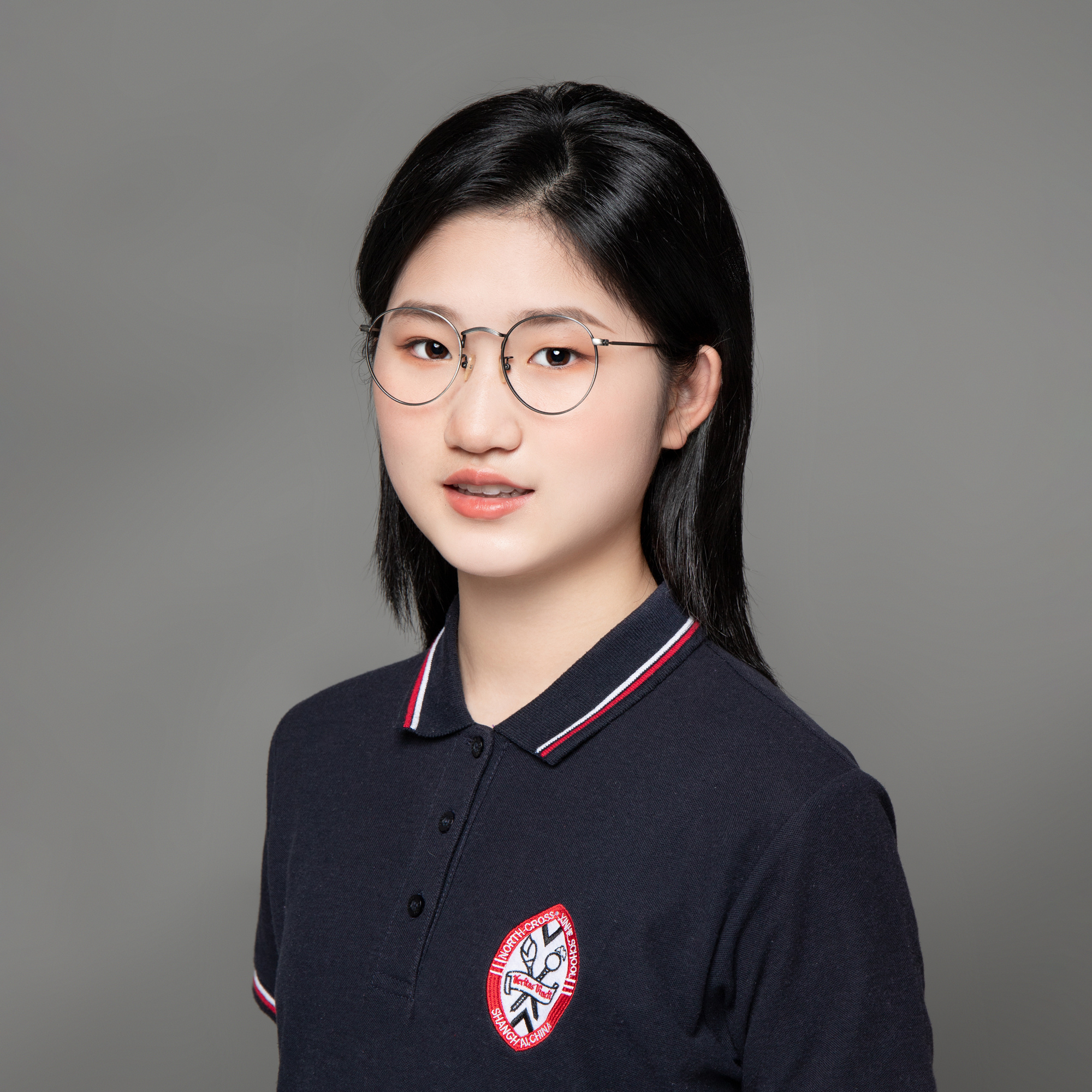 Girl with dark hair and glasses in a blue polo shirt on gray background