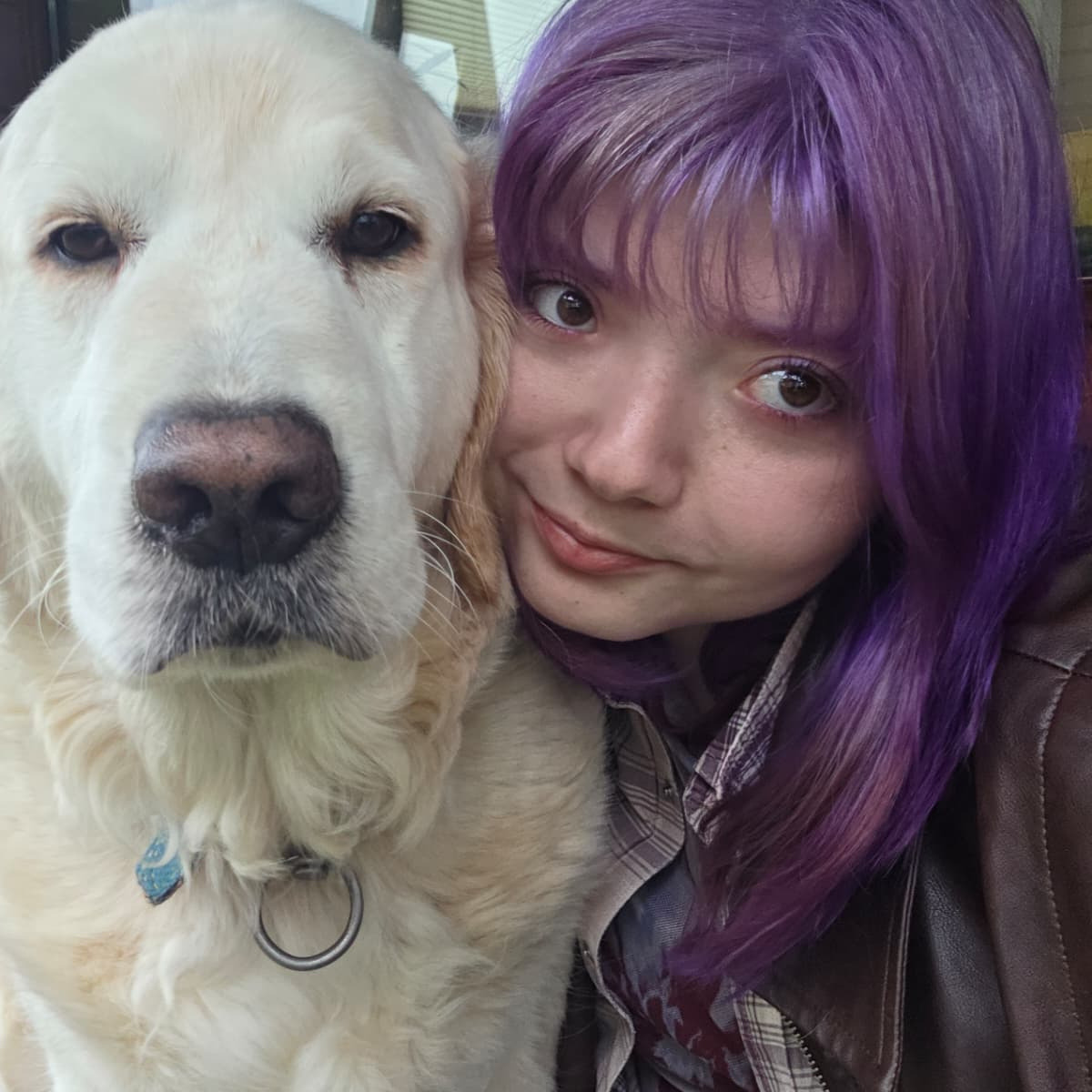 Girl with purple hair smiles next to golden retriever dog
