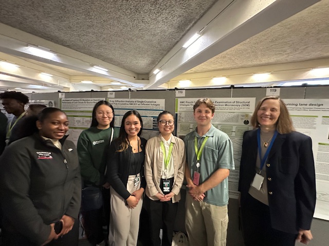 Six people smiling in front of a poster