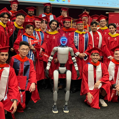 a group of graduates in red and caps and gowns pose next to a silver robot
