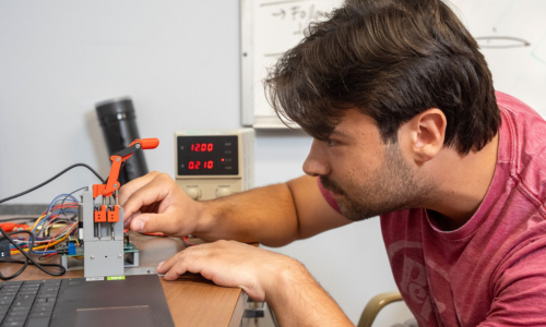 Nick Baiata works on a small robot next to a laptop