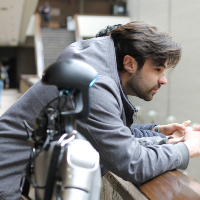 Nick Baiata gazes over the edge of a balcony with a silver robot standing next to him