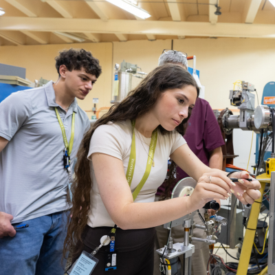 Samantha works on an engine with fellow student standing by watching