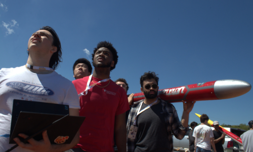 Members of the SBU Rocket Team look up at the sky during the launch. One member holds the Ultra-Deinde Rocket on his shoulders