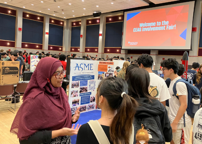 Students discuss the ASME club at a crowded engineering involvement fair beneath a screen welcoming attendees to the CEAS Involvement Fair.
