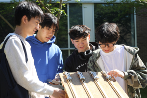 Mechanical Engineering students work together outdoors on a hands-on engineering project, examining and adjusting a prototype device while collaborating on design and problem-solving activities.