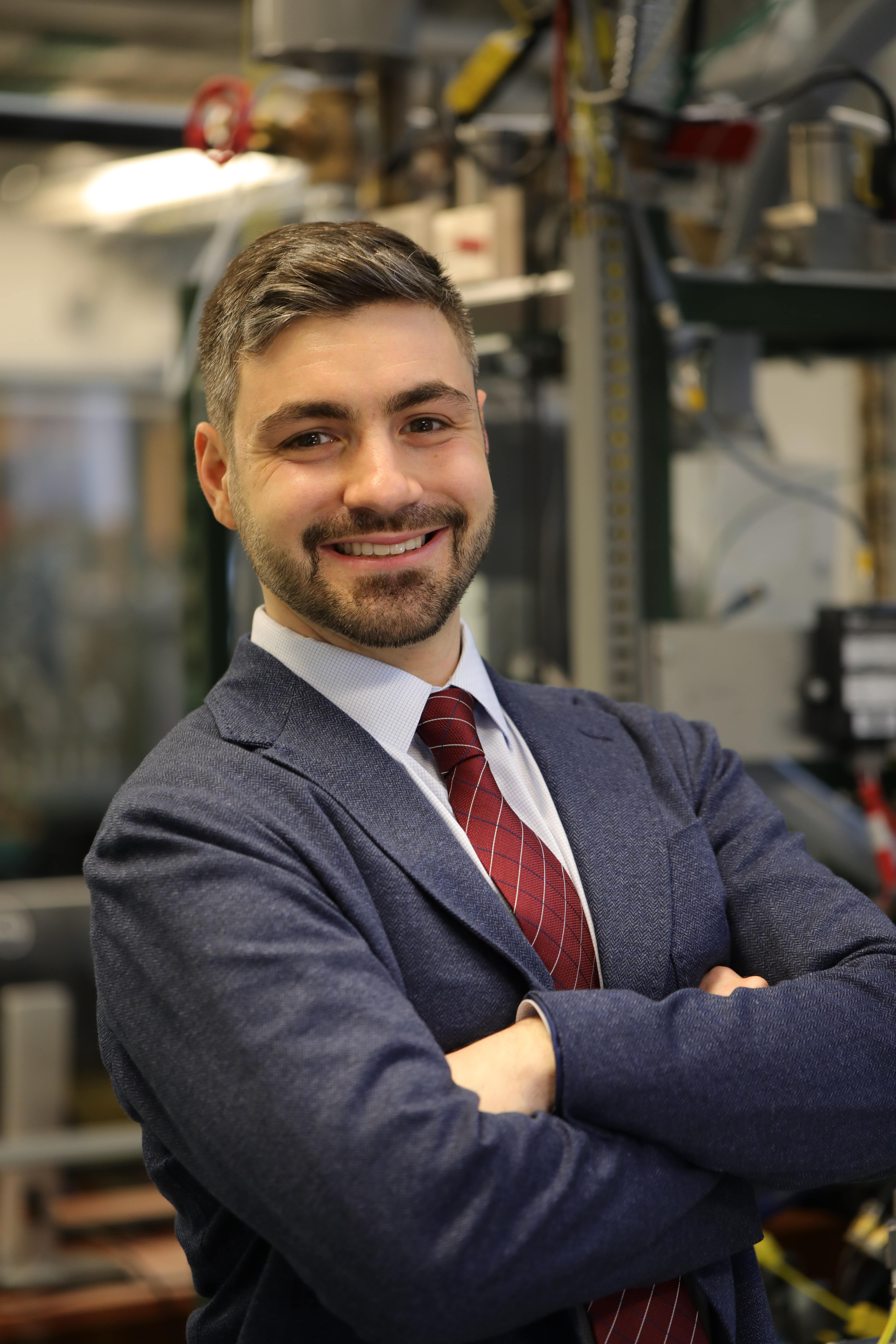 Headshot of Dimitris Assanis standing in front of machinery 