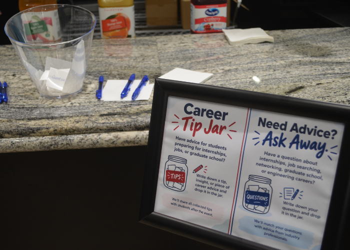 Framed “Career Tip Jar” and “Need Advice? Ask Away!” sign beside a clear jar, pens, and paper slips on a countertop.