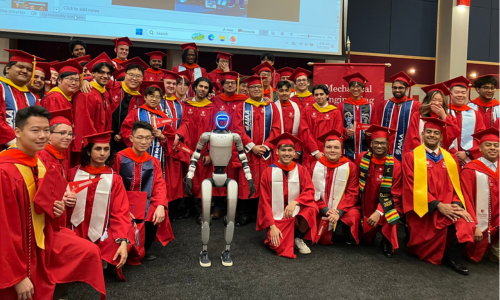 Graduates in red caps and gowns pose with a silver robot