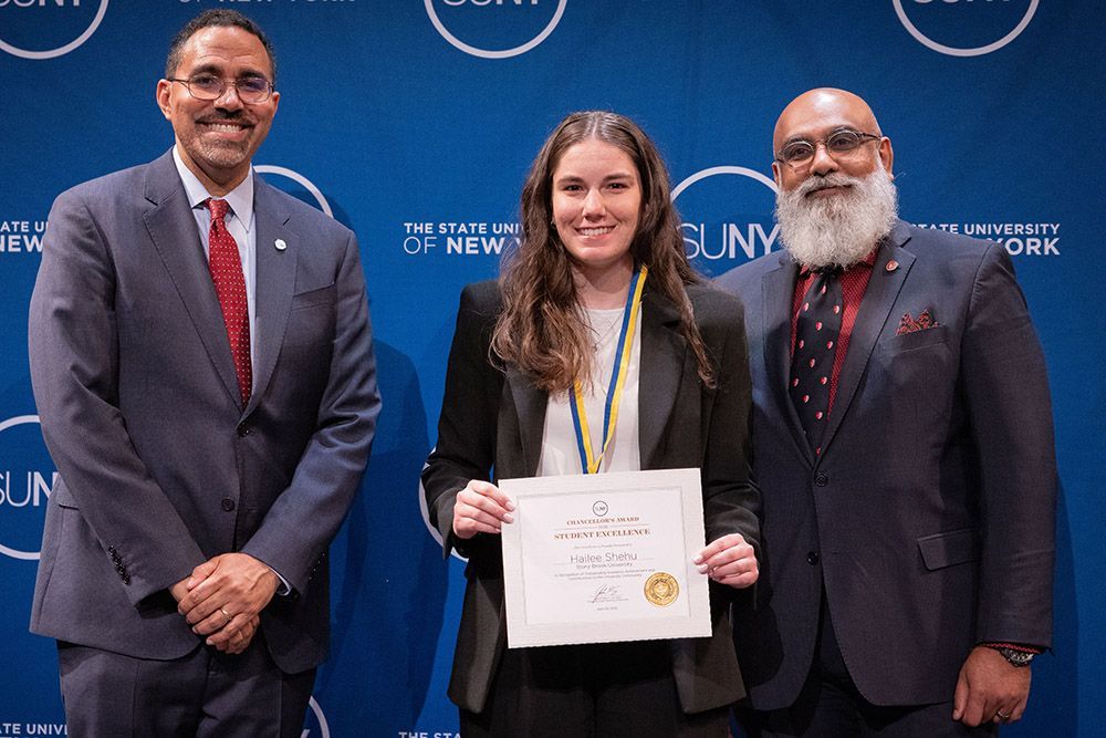 Hailee Shehu poses with her award, flanked by SBU Faculty