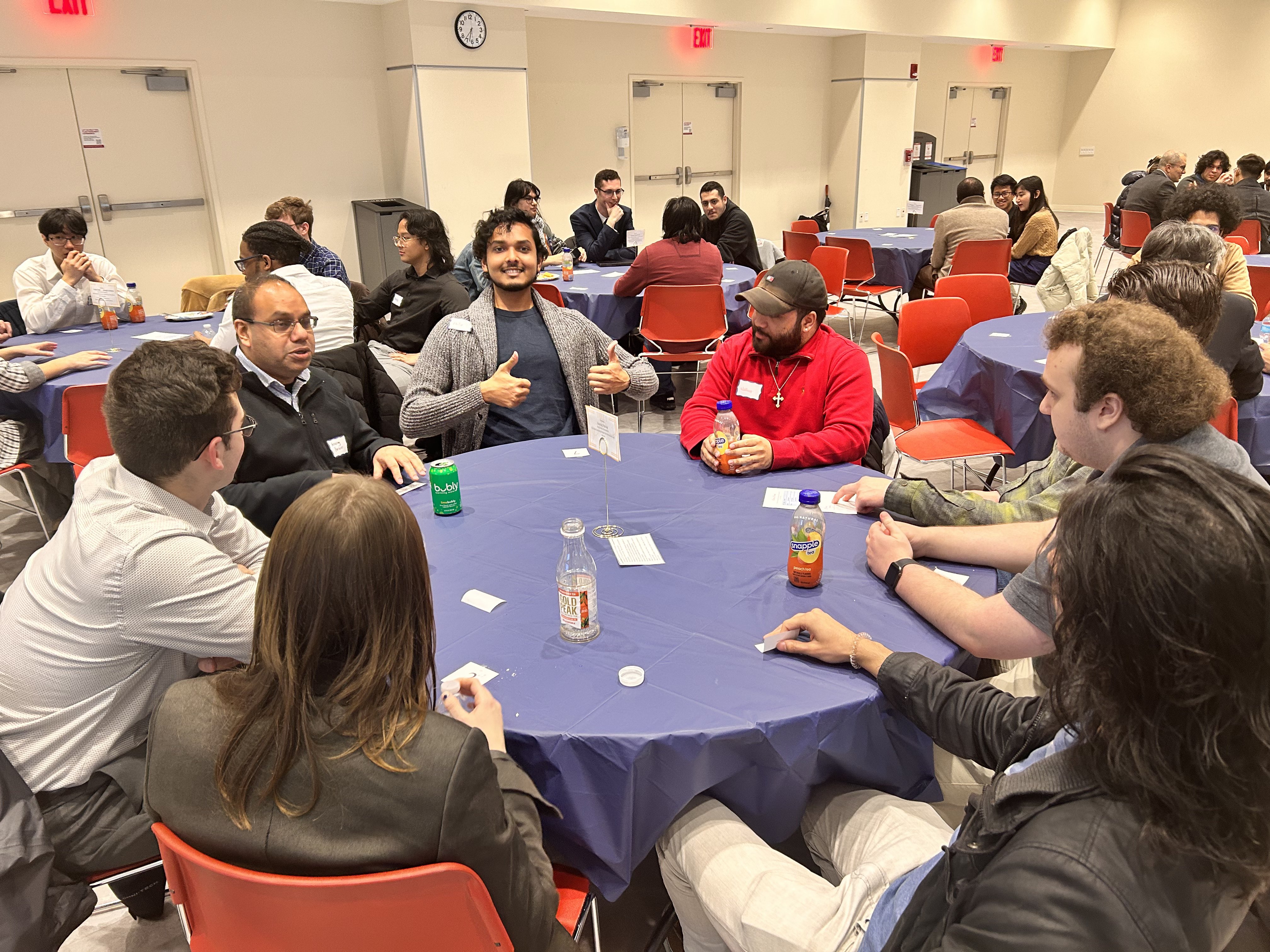 Students and faculty seated at a round table with a blue tablecloth