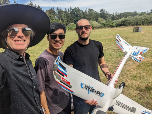 Three researchers stand in a field holding a lattice-based UAV