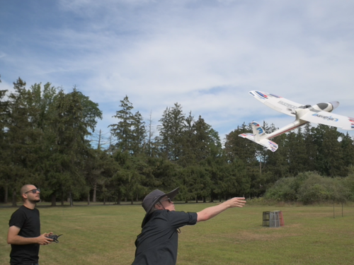 Two researchers test a UAV drone in a field; one is launching the drone while the other operates a remote control.
