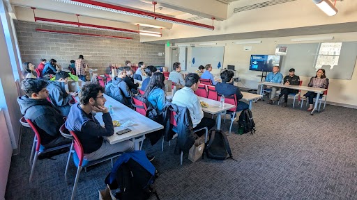 People seated at tables with panelists seated at the front of the room. 