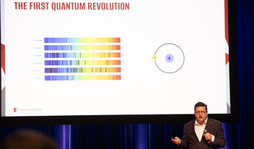 P. Scott Carney presents information on "THE FIRST QUANTUM REVOLUTION" with a projection of spectral data and an illustration of an atom.