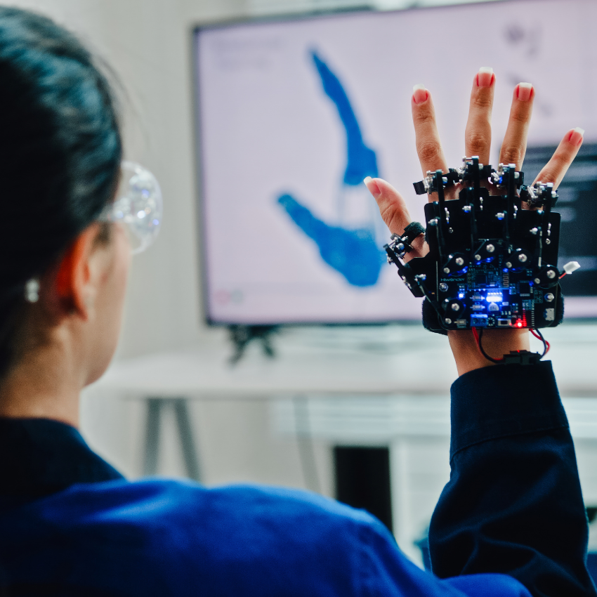 Student wearing a sensor-equipped robotic glove while interacting with a computer display showing hand-motion tracking.