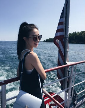Jenny Jeng; Girl wearing hair in ponytail and sunglasses while standing by the railings of a boat on the sea, with a American Flag nearby