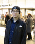 Yifang Cao; Guy wearing glasses, knit cap, and a black jacket with people walking behind