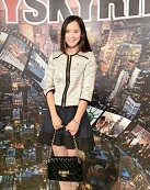 Yuli Ma; Girl with medium black hair standing against a decorated wall and holding a bag