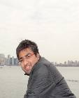 Minesh Javiya; guy wearing glasses and fringed up hair, leaning against railing by the water